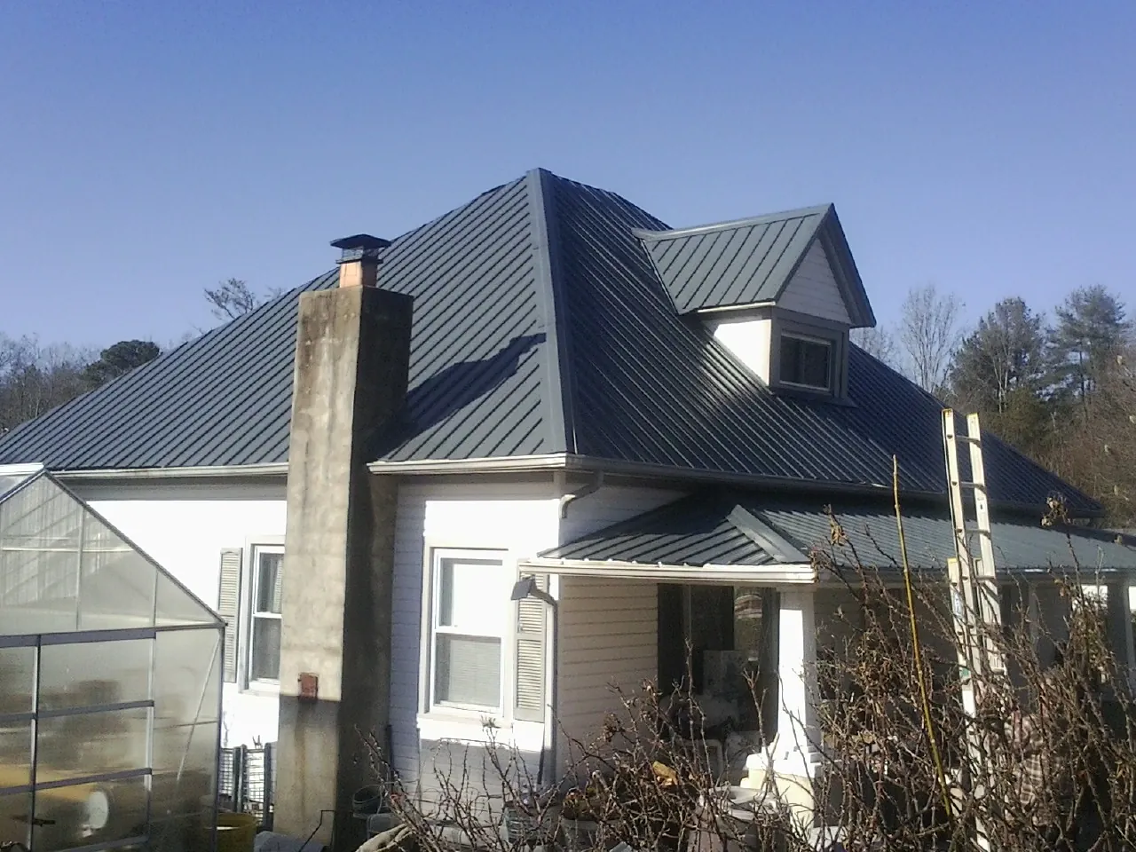 Dark blue standing seam metal roof on a white farmhouse with dormer — Slate & Tile Roof Repair by Roofing Brothers in Maybell
