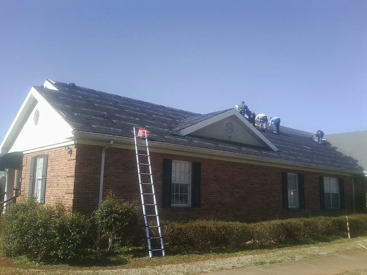 Crew tearing shingles off a brick ranch roof with a ladder set — Emergency Roof Repair work by our crew in Maybell