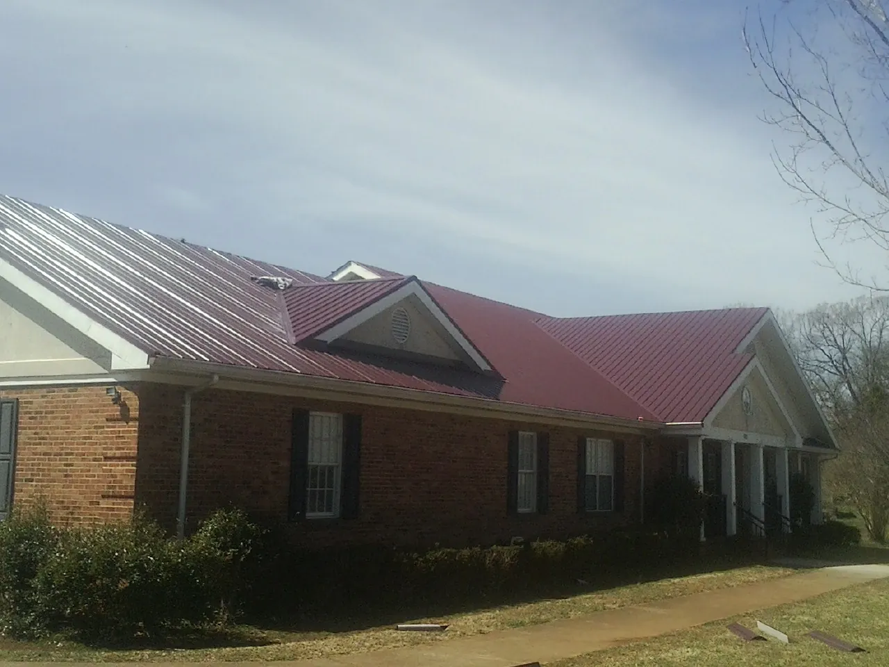 Red metal roof with gabled entries on a long brick building, from a Hail Damage Roof Repair job in Maybell