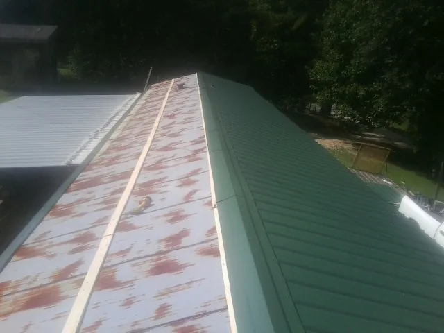 Old rusted panels beside newly installed green metal roofing — Wind Damage Roof Repair by Roofing Brothers in Maybell