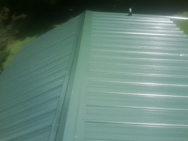 New green metal panels meeting at the ridge of a roof — Flat Roof Repair work by our crew in Maybell