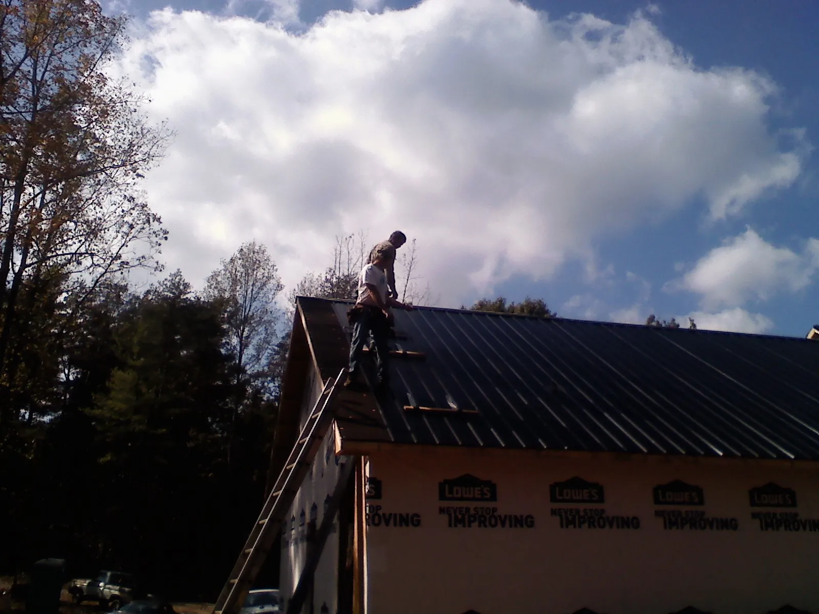 Roofer fastening dark metal panels high against a cloudy sky, from a Roof Inspection job in Maybell