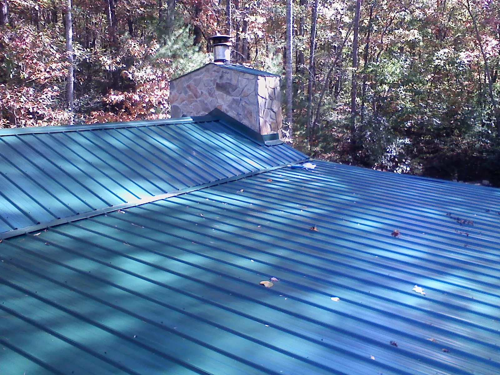New green metal roof and stone chimney surrounded by autumn woods in Maybell