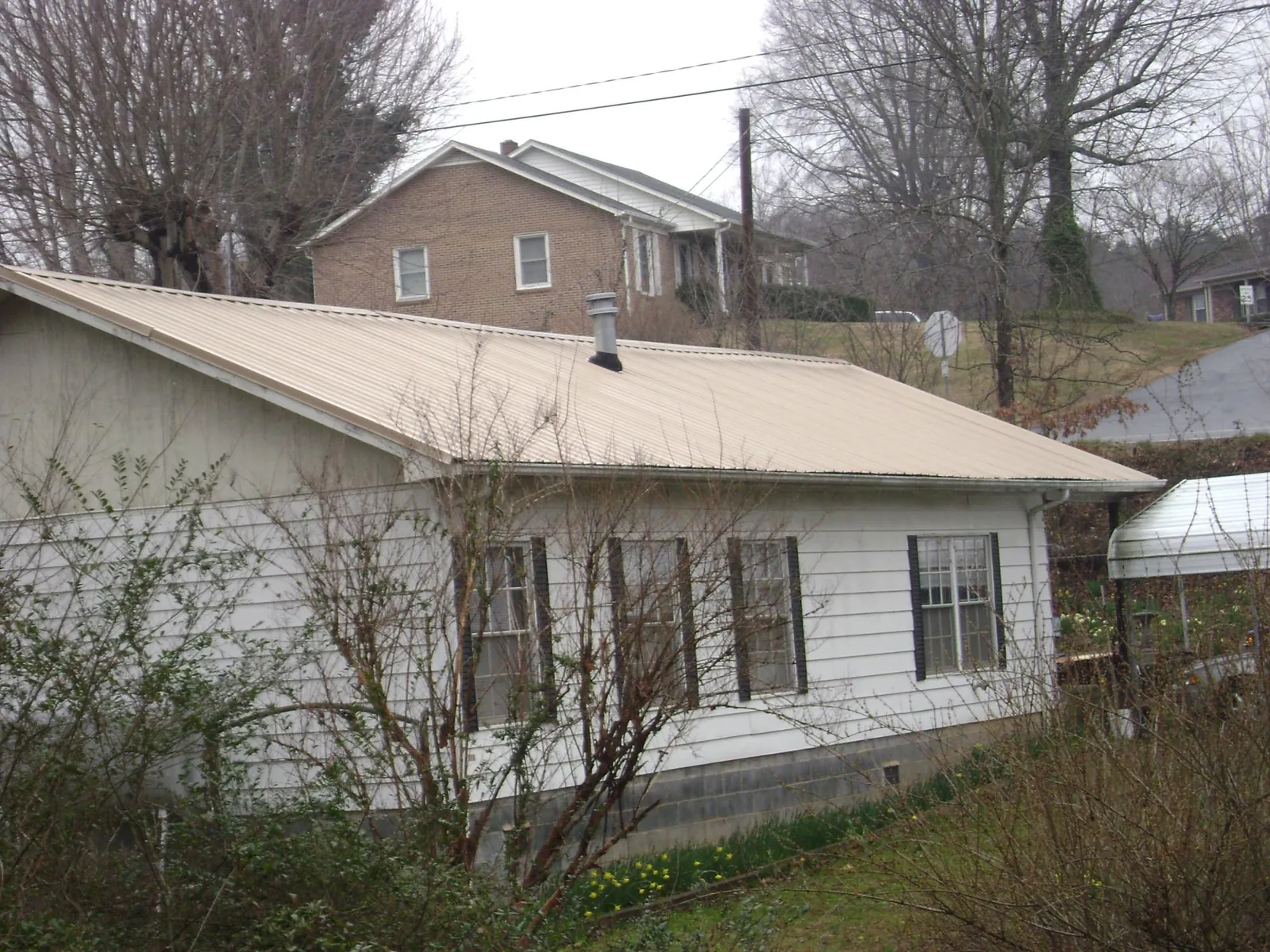 Tan metal roof on a white sided house set into a hillside — Commercial Roofing by Roofing Brothers in Maybell
