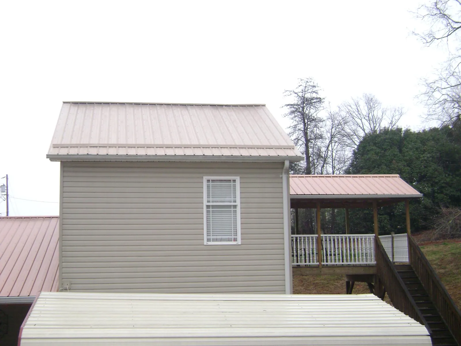 Tan metal roofs on a two story addition and attached porch, from a Roof Replacement job in Maybell